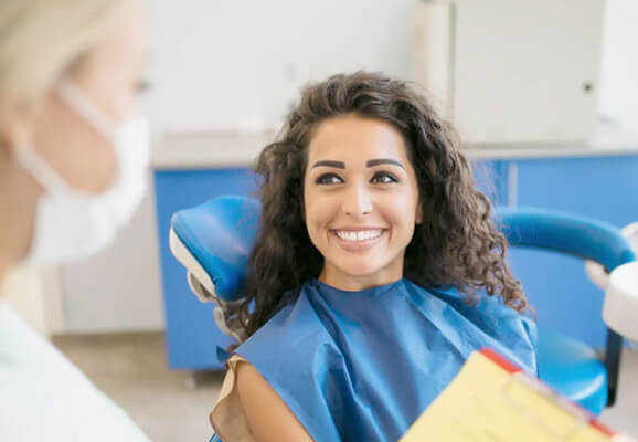 Smiling woman in dental bib reclines in dentist chair during examination.