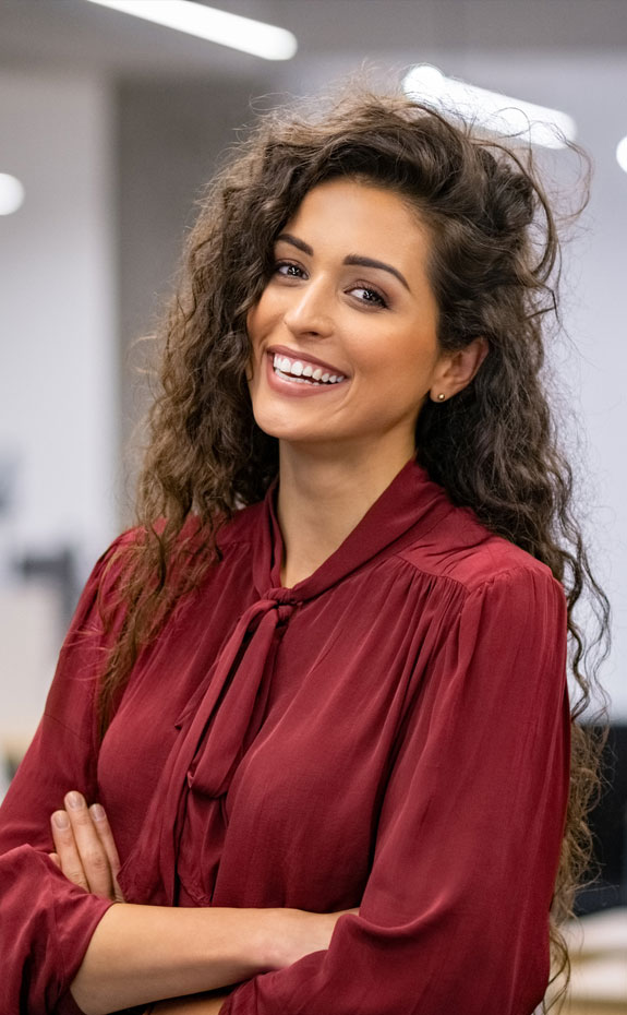 Woman in burgundy blouse smiling at camera in modern dental office setting.