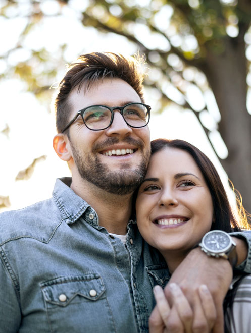 Smiling couple outdoors wearing casual clothing in natural daylight setting.