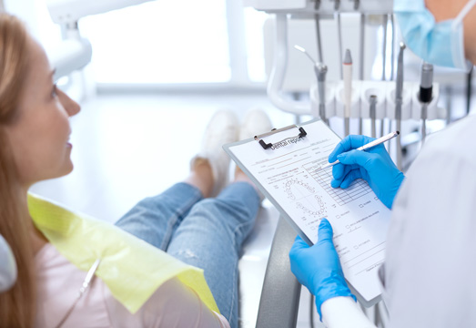 Dentist in blue gloves examining patient's teeth using dental tools in clinical setting.