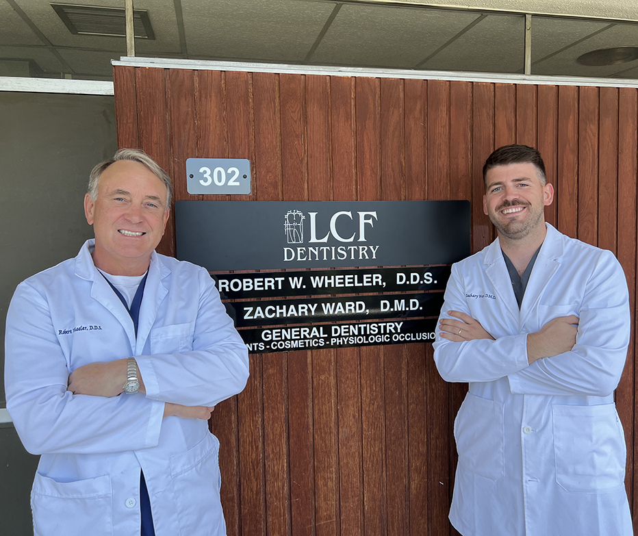 Two dentists in white coats standing beside LCF Dentistry office sign with names displayed.