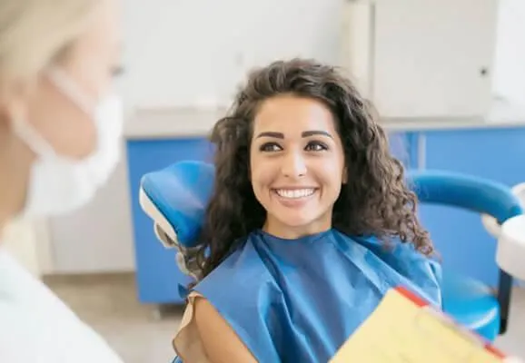 Woman in dental bib smiling in dentist's chair during examination at dental office.