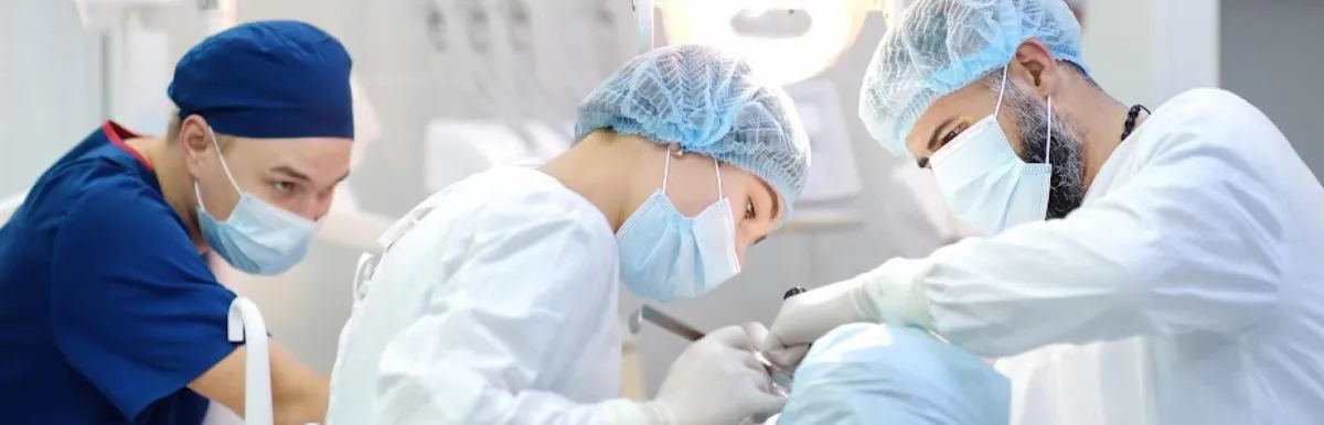 Dental professionals in surgical attire performing a procedure in a clinical operating room.